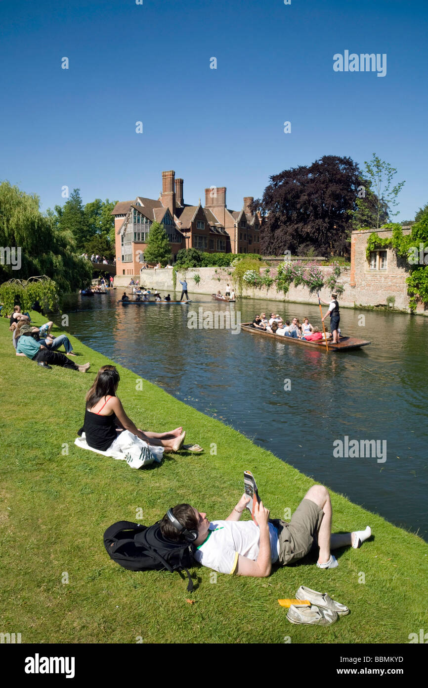 People sitting on the banks of the River Cam at Clare College, Cambridge, watching the punting on a summers day Stock Photo