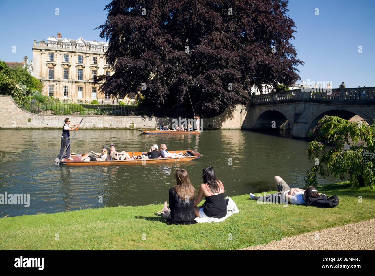 People sitting on the banks of the River Cam at Clare College, Cambridge, watching the punting on a summer day, Clare College, Cambridge University UK Stock Photo