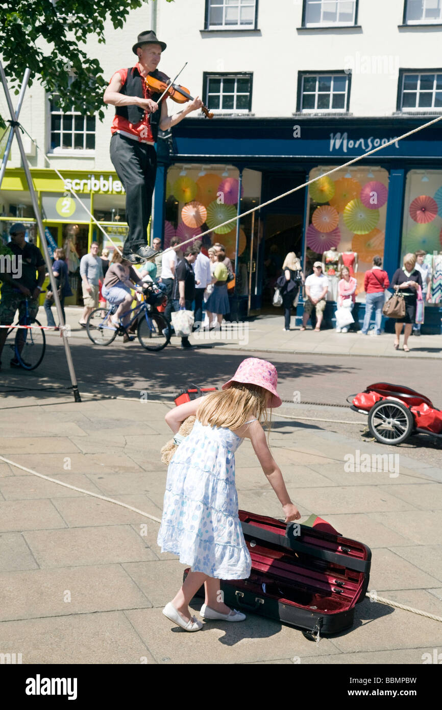 A young girl gives money to a violin-playing tightrope-walking street entertainer, Sidney Street, Cambridge, UK Stock Photo