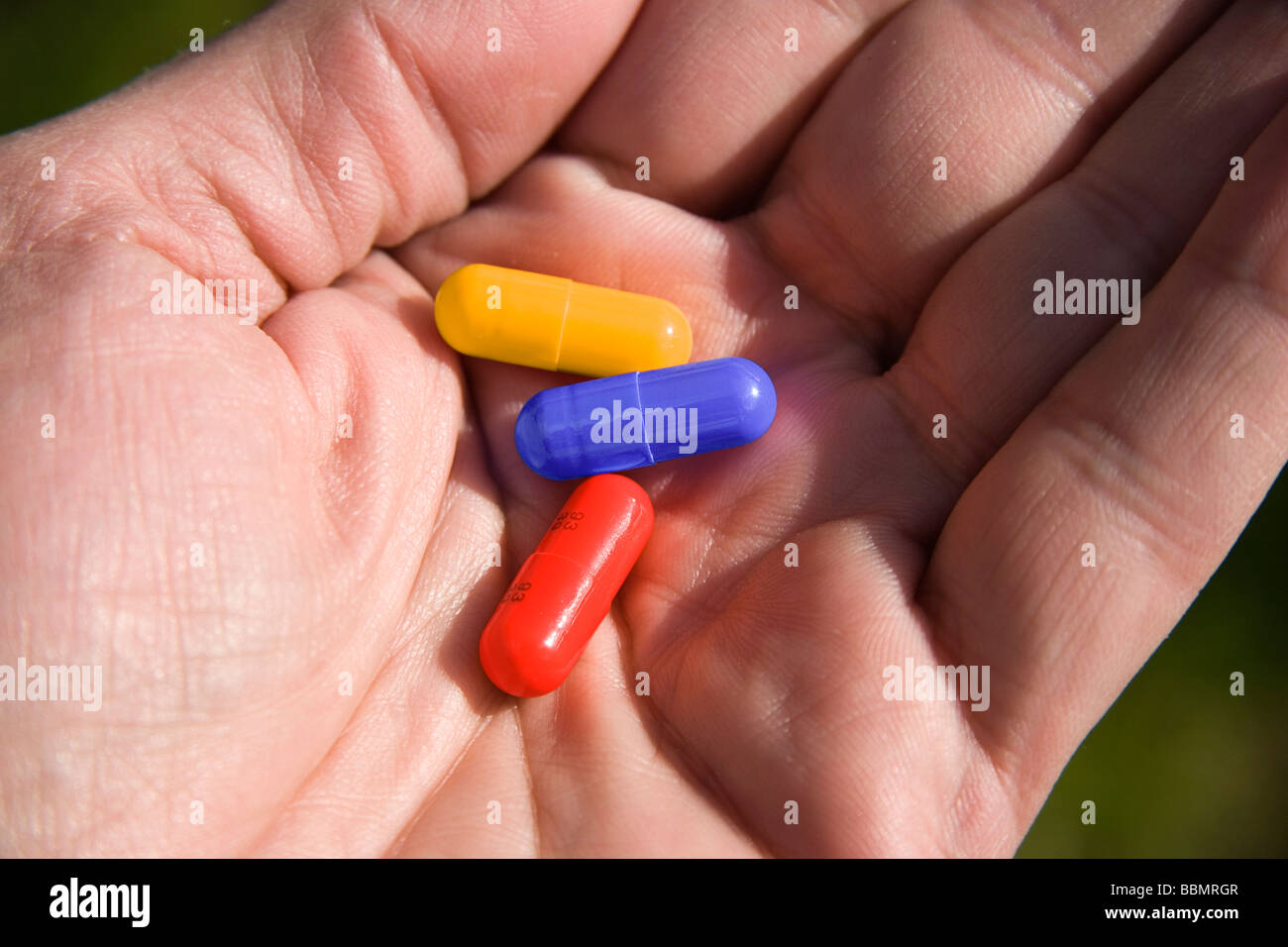 Three colourful medicine capsules in the palm of a hand Stock Photo