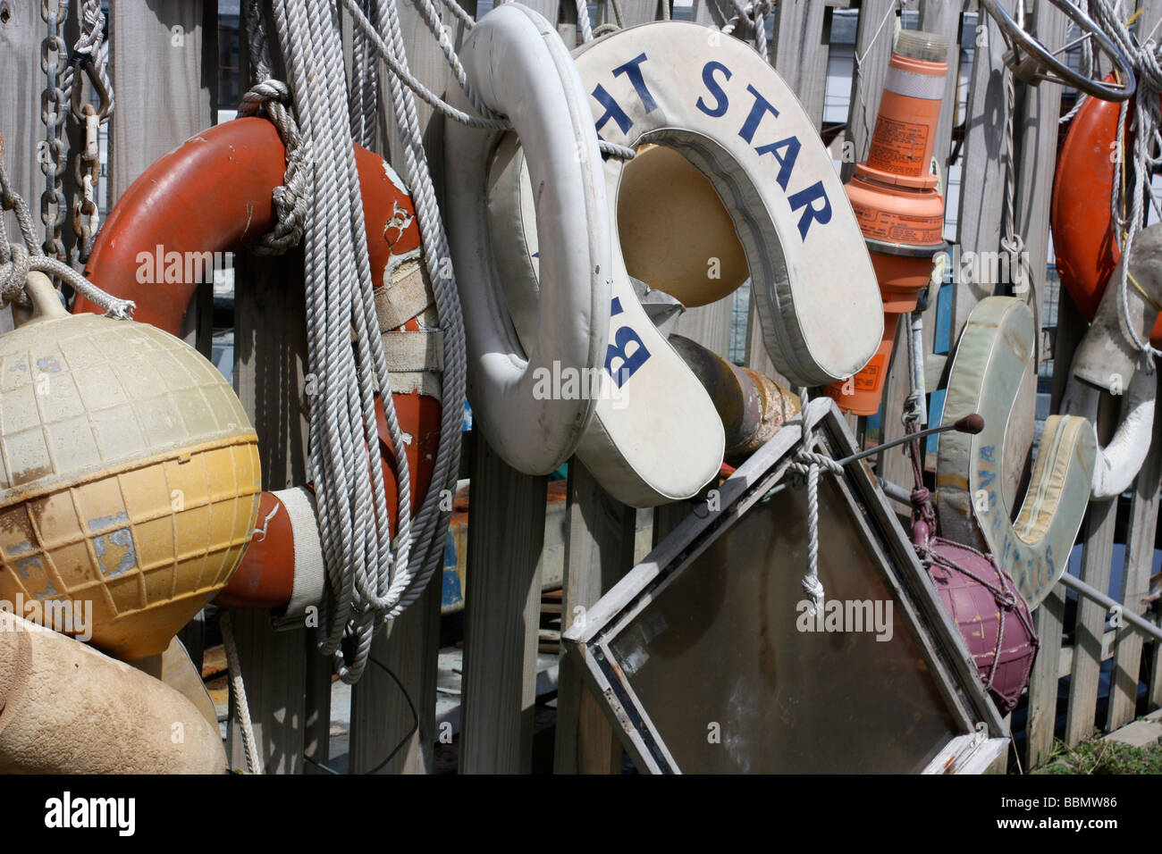 A collection of nautical objects used for sailing tied to a fence including bouys life rings rope beacon chain and wheel Stock Photo