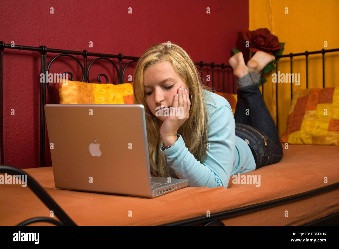 Young woman lying on a bed working on a laptop Stock Photo