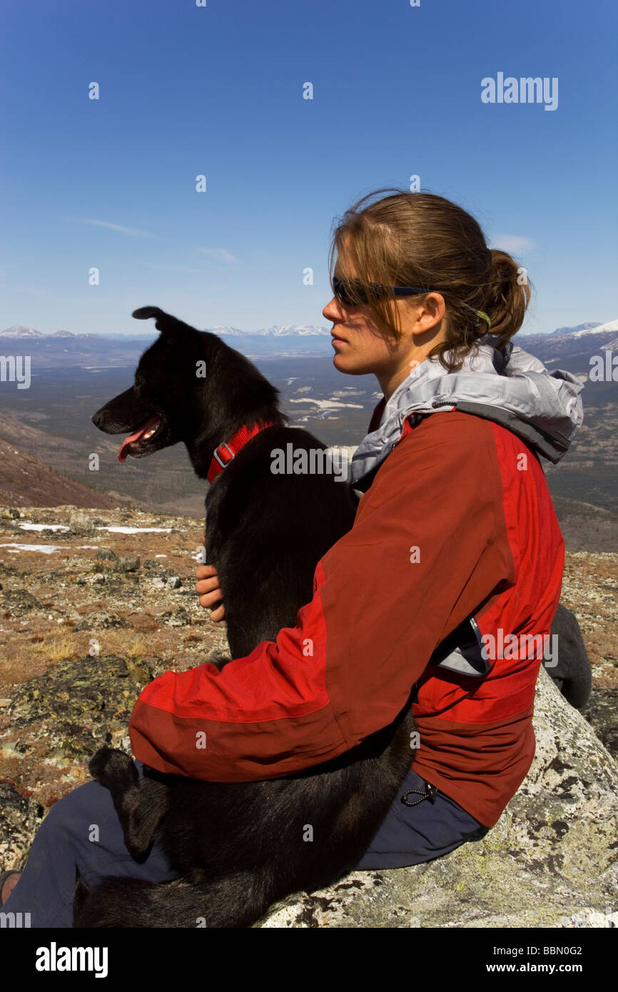 Hiker resting, sitting on a rock, young woman with dog, sled dog, Alaskan husky, mountains behind, Kusawa Ridge, Yukon Territor Stock Photo