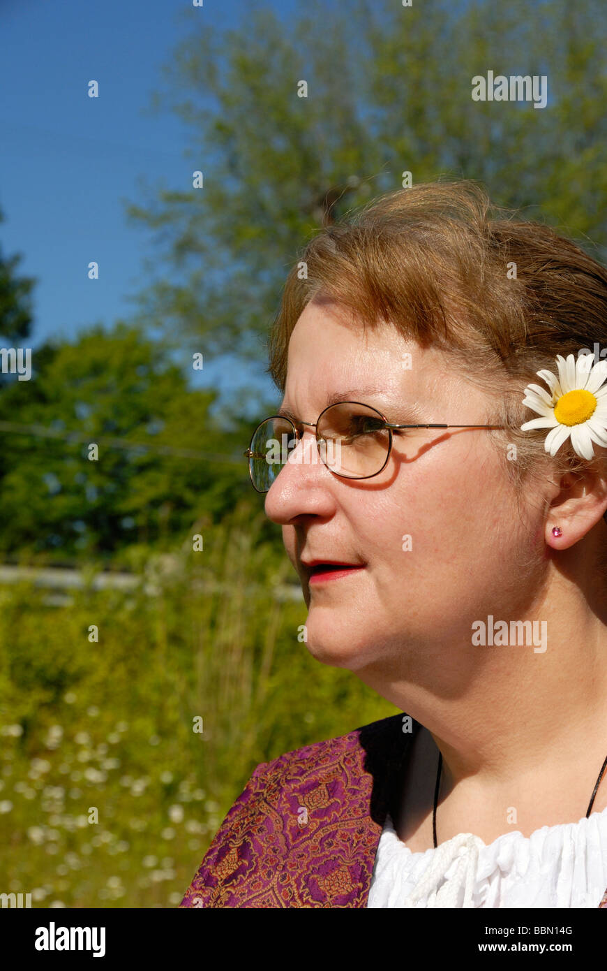 woman in field with flower in her hair wearing glasses Stock Photo
