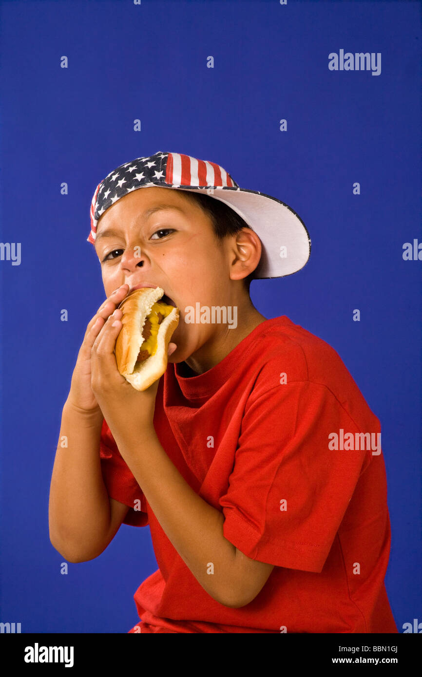 Portrait of young Hispanic boy 7-9 year old wearing July 4th stars stripes hat holiday eating hotdog MR  © Myrleen Pearson Stock Photo
