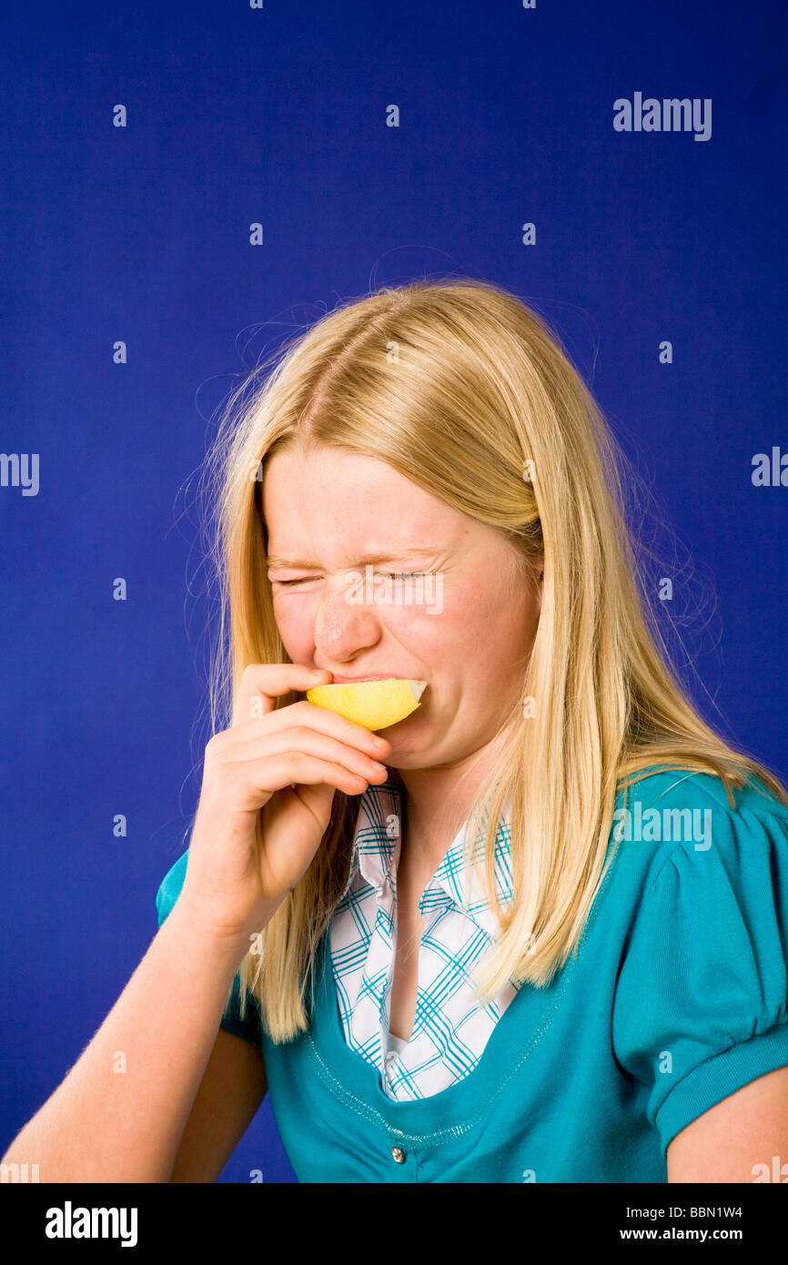 Portrait of young girl eating sour lemon making facial pulling face person people reaction eyes squeezed shut cut out US USA  United States America US Stock Photo