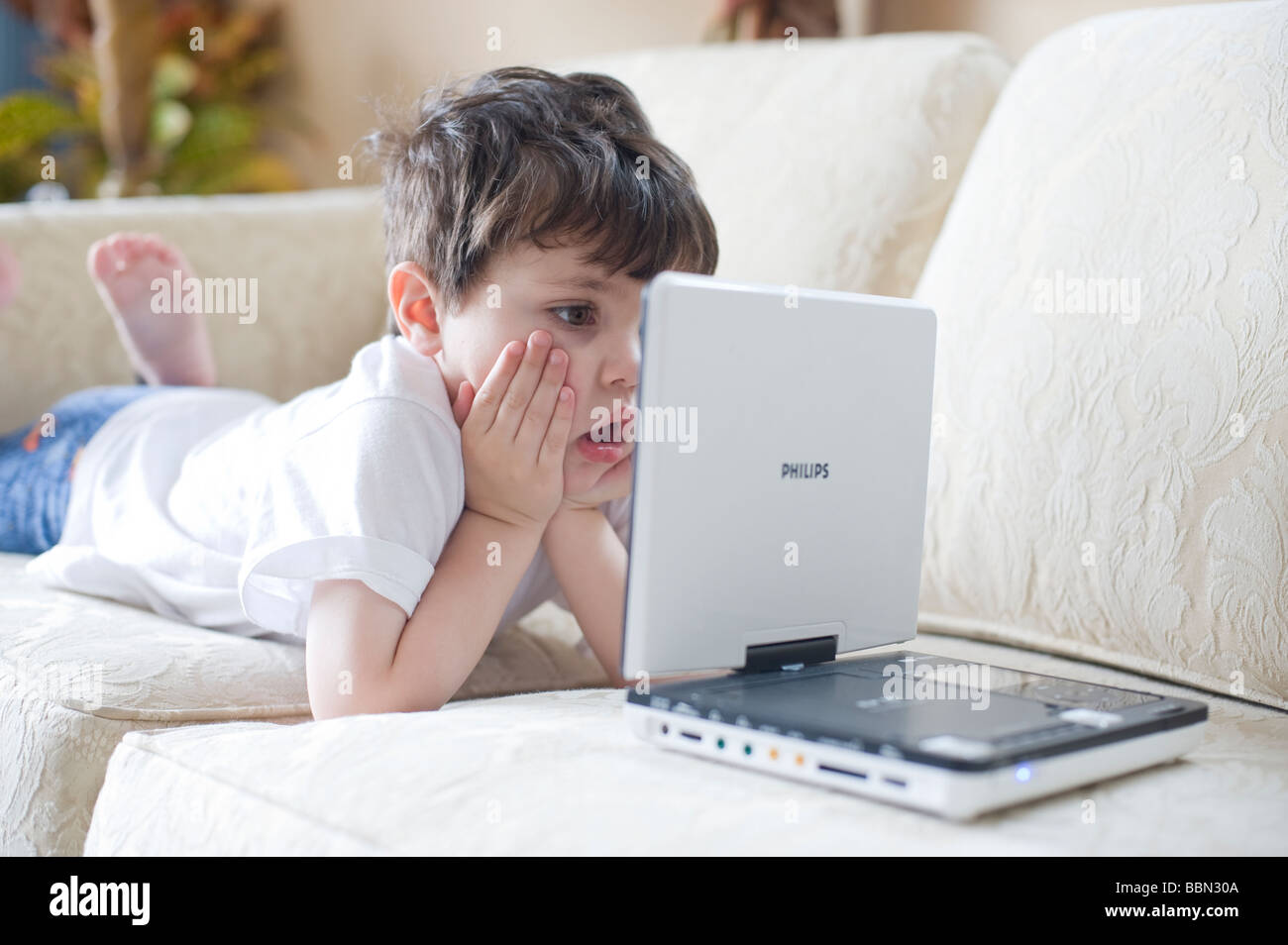 Three year old hispanic boy is mesmerized by a 'Wiggles' DVD playing on a portable DVD player Stock Photo