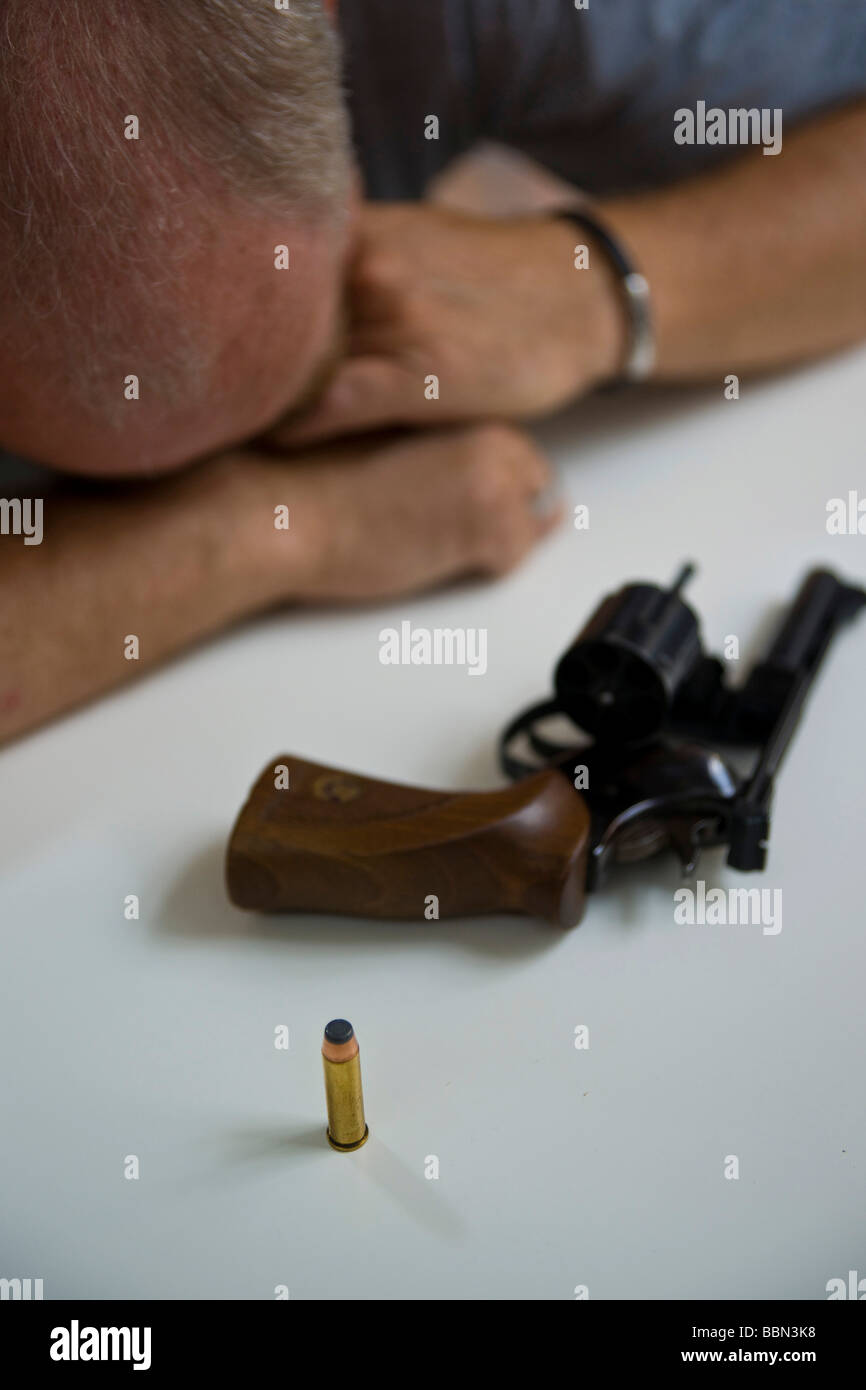 A revolver with one cartrige lying on the table in front of a desperate man Stock Photo