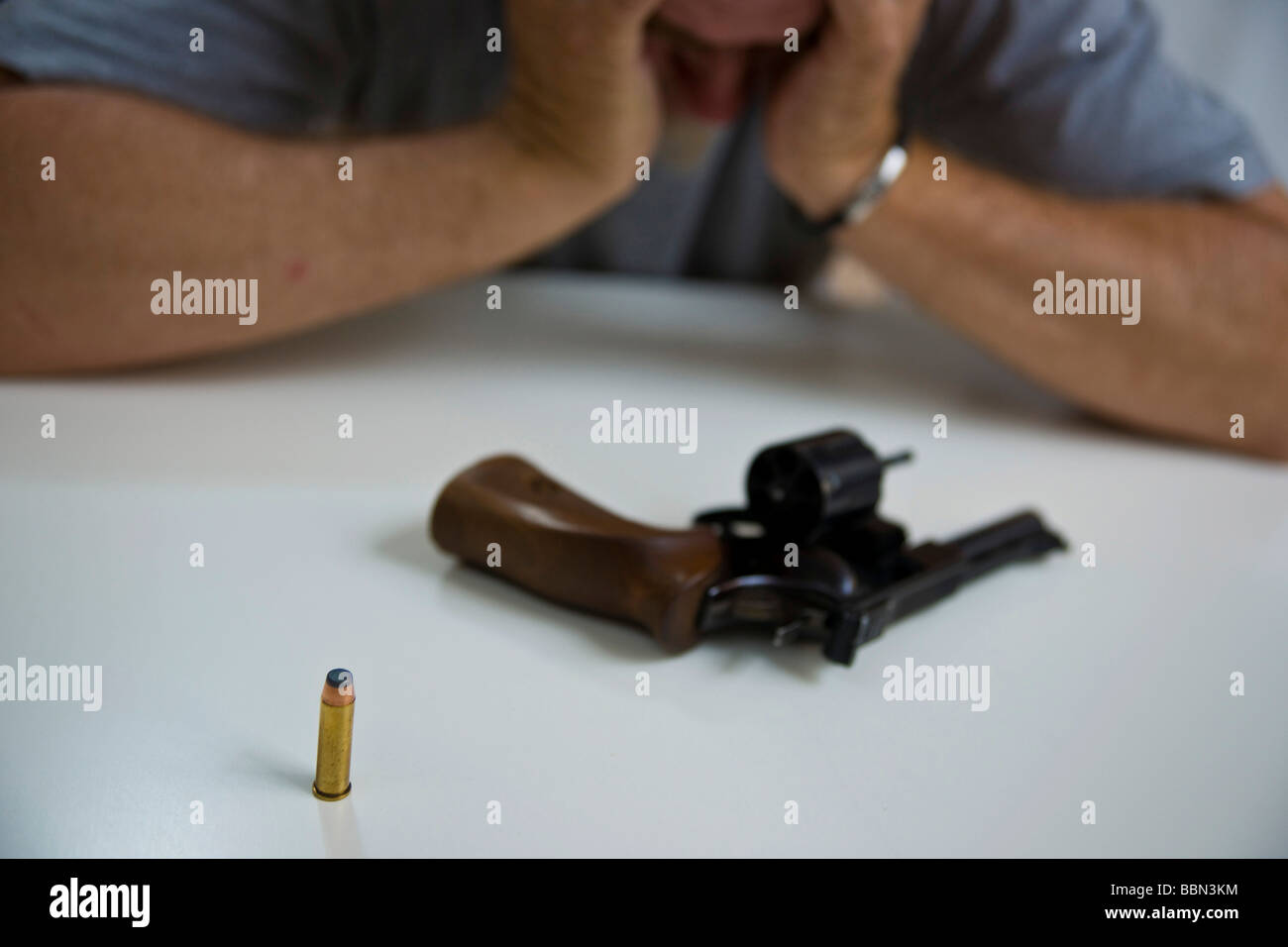 A revolver with one cartrige lying on the table in front of a desperate man Stock Photo