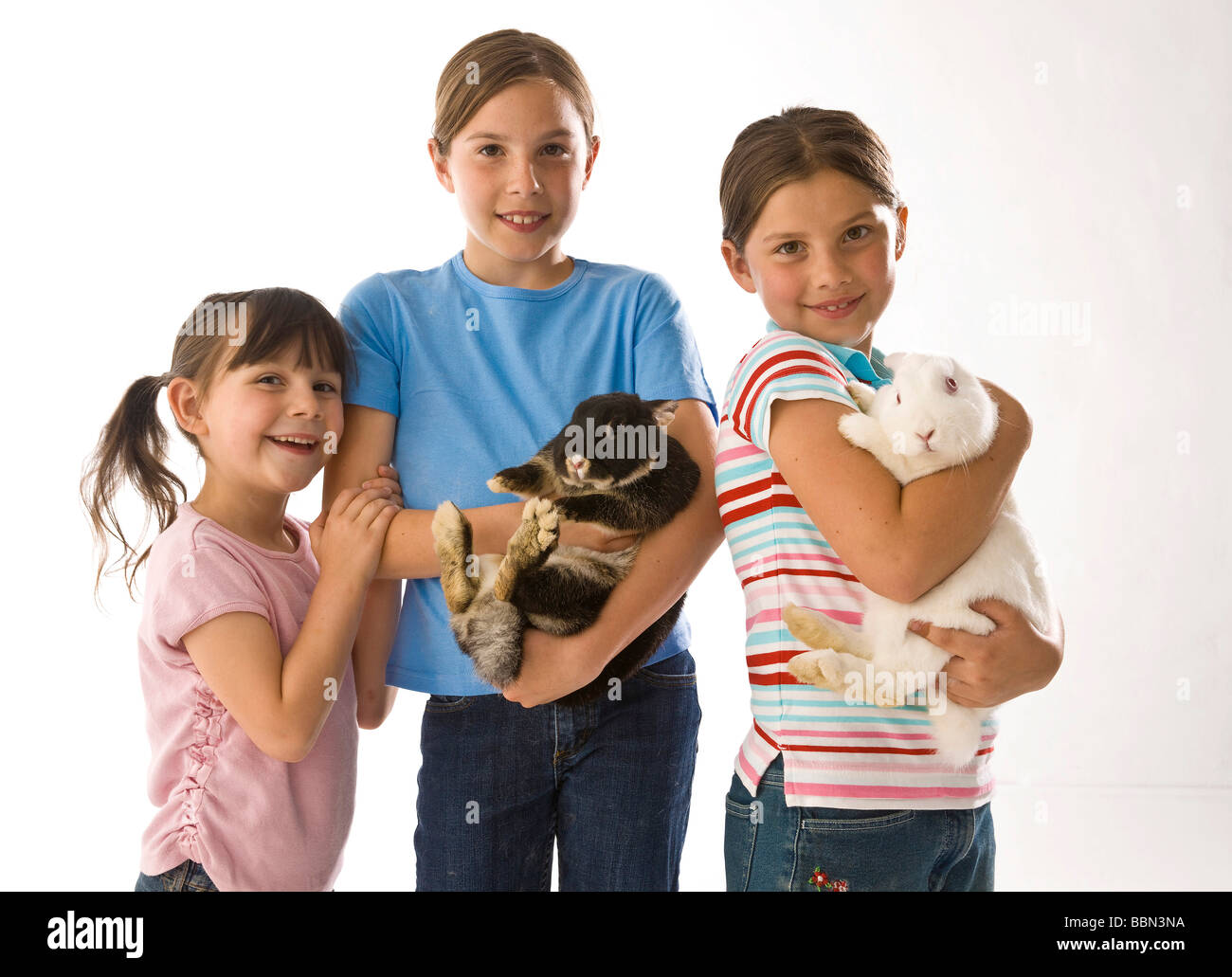 A group of three girls, the two older ones holding a rabbit in their arms Stock Photo