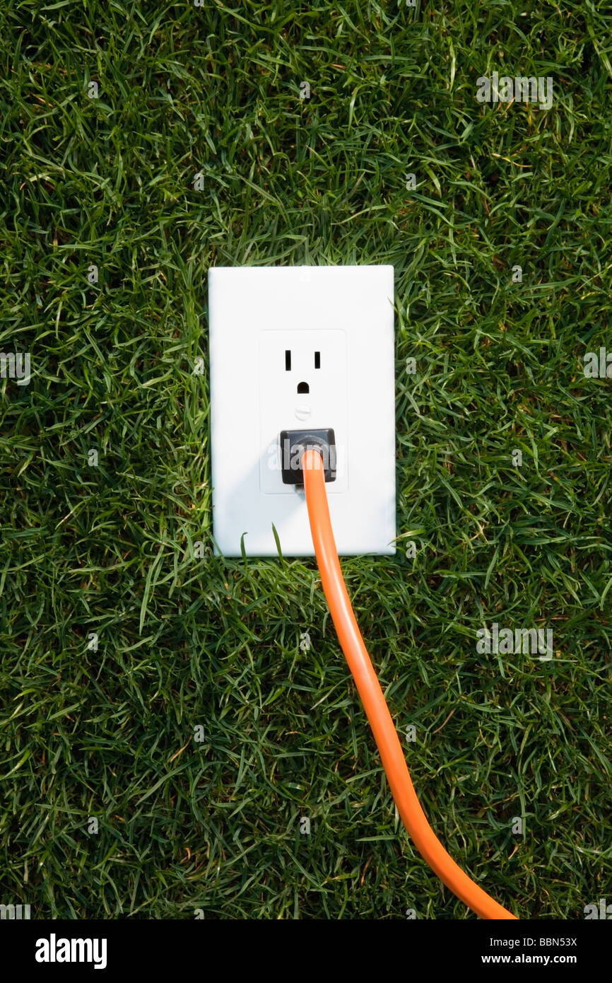 Electrical outlet in grass with extension cord plugged in Stock Photo