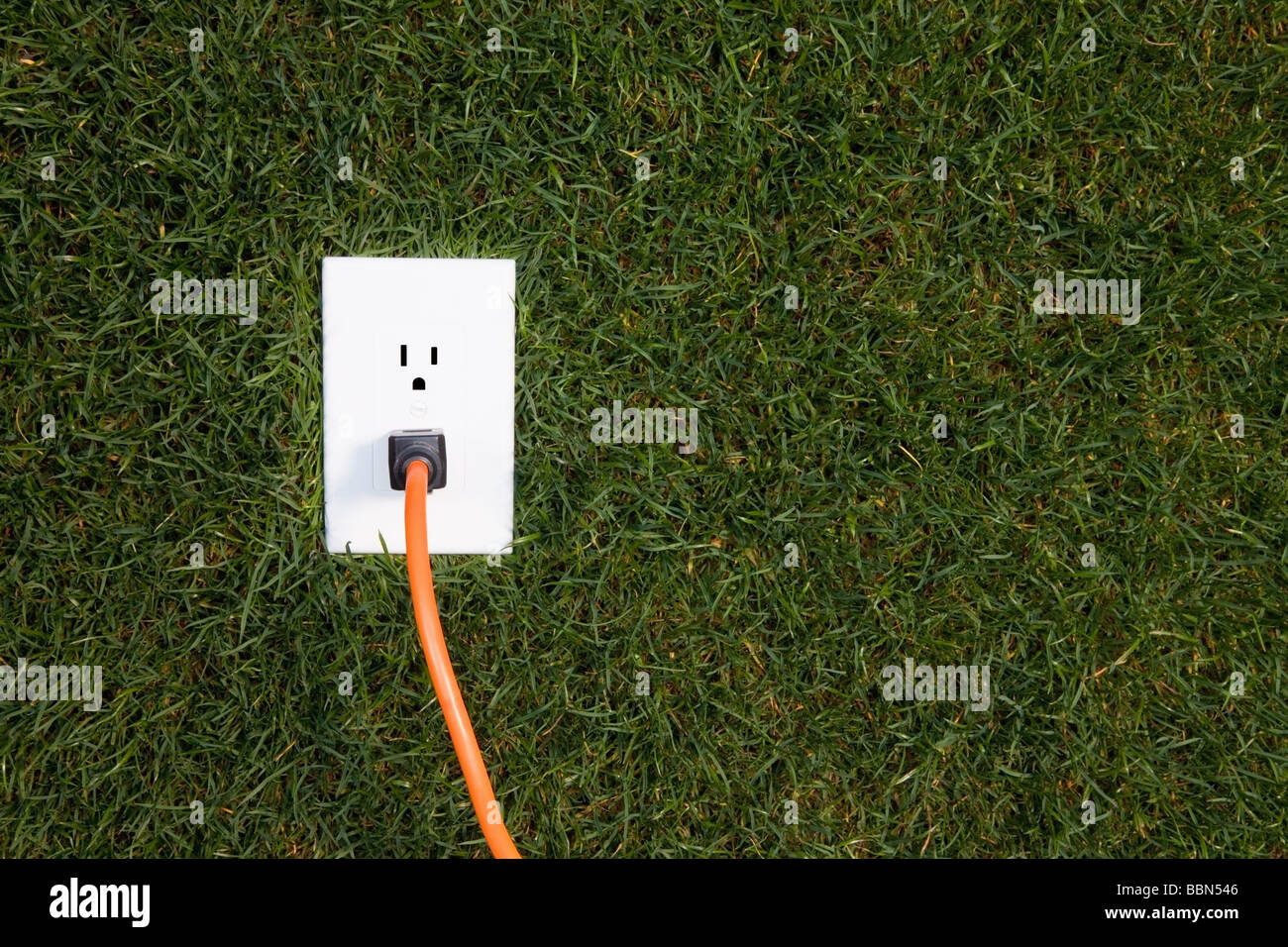 Electrical outlet in grass with extension cord plugged in Stock Photo