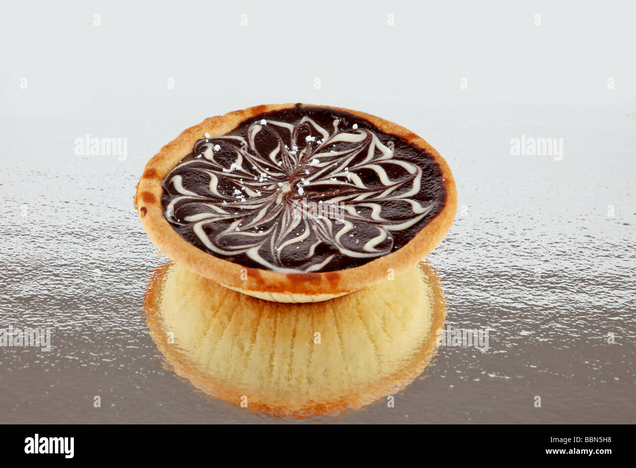 Caramel fudge tart with chocolate decorated top on a reflective surface Stock Photo
