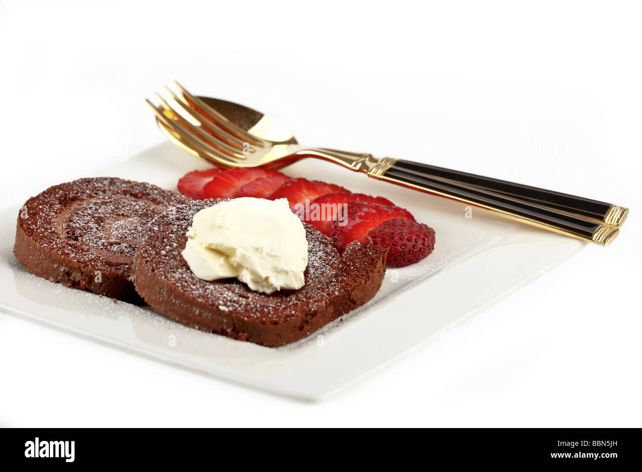 Chocolate swiss role with cream and strawberries on aplate with fork and spoon Stock Photo
