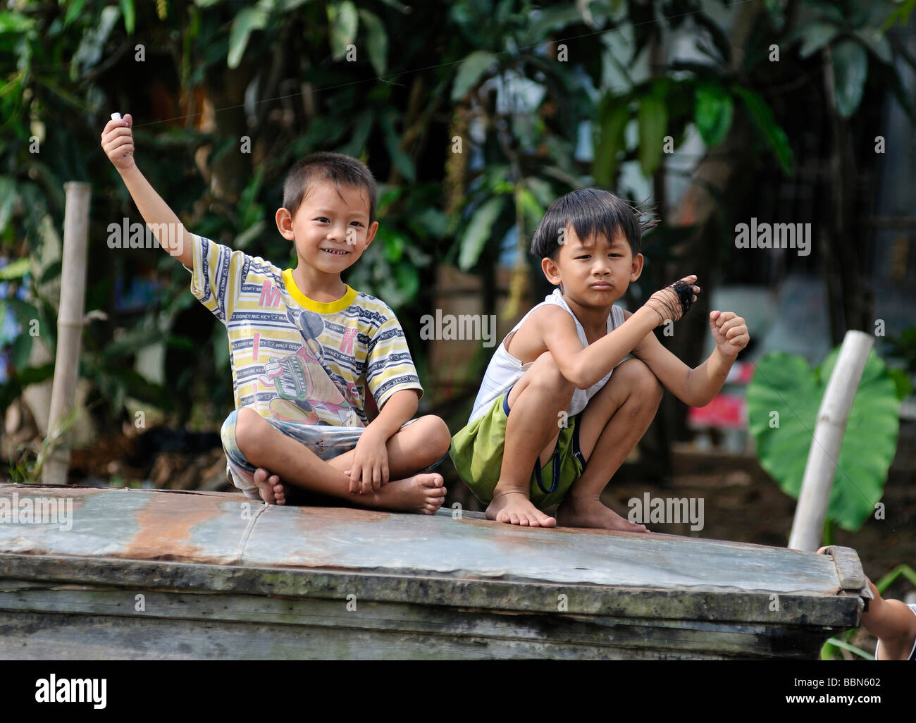 Two children sitting on a wooden roof and playing with thin strings of kites, Vietnam, Asia Stock Photo
