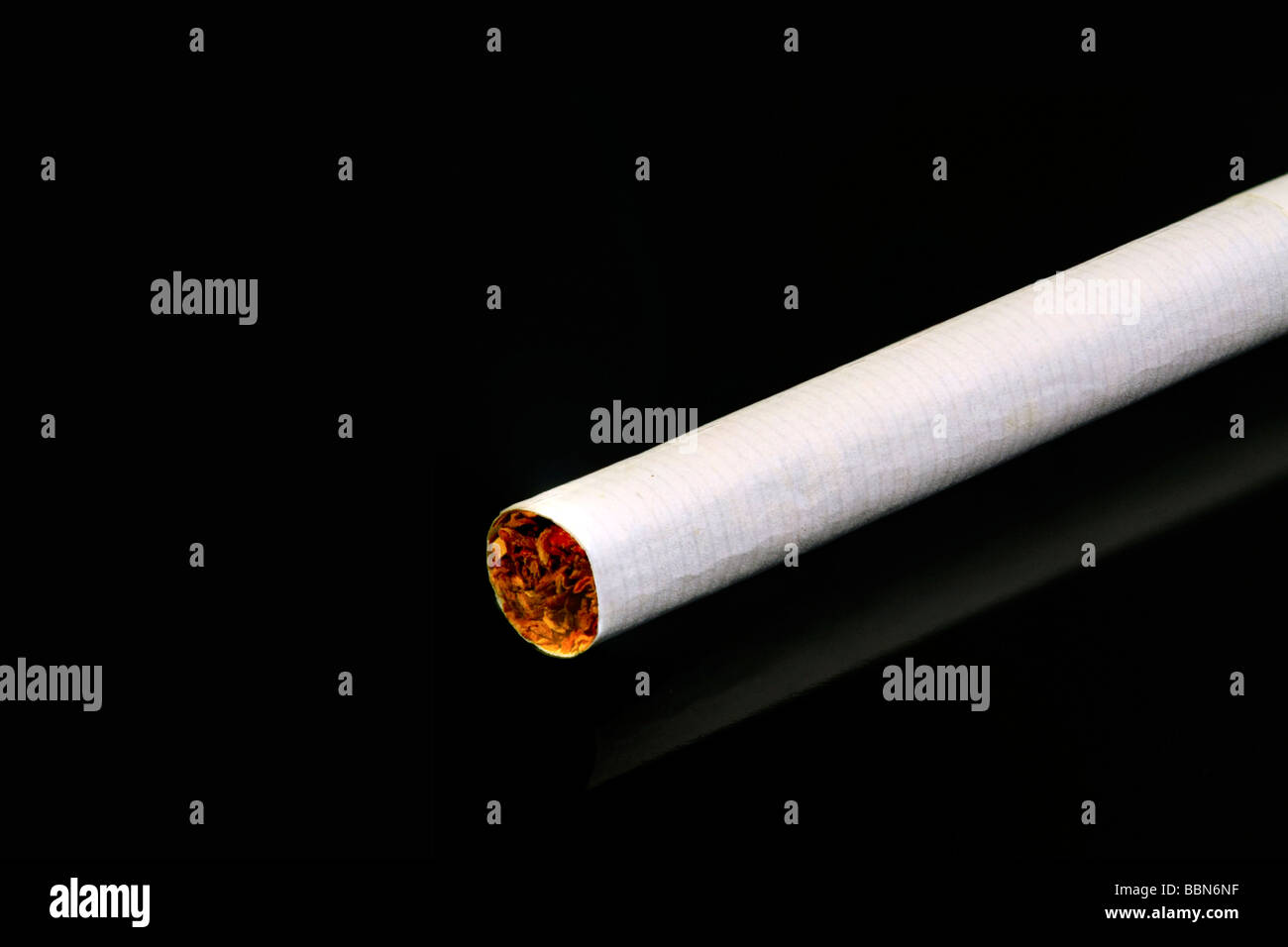 One single white cigarette on a black reflective surface Stock Photo