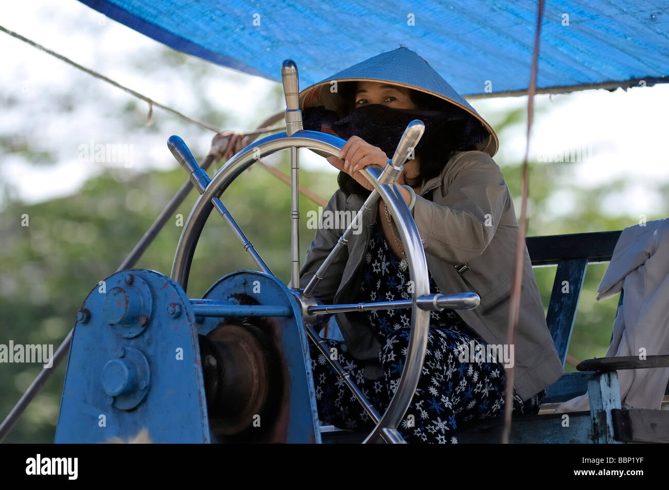 Woman with a traditional hat, cone-shaped hat made of palm leaves, steering a steering wheel at the Mekong, Can Tho, Mekong Del Stock Photo
