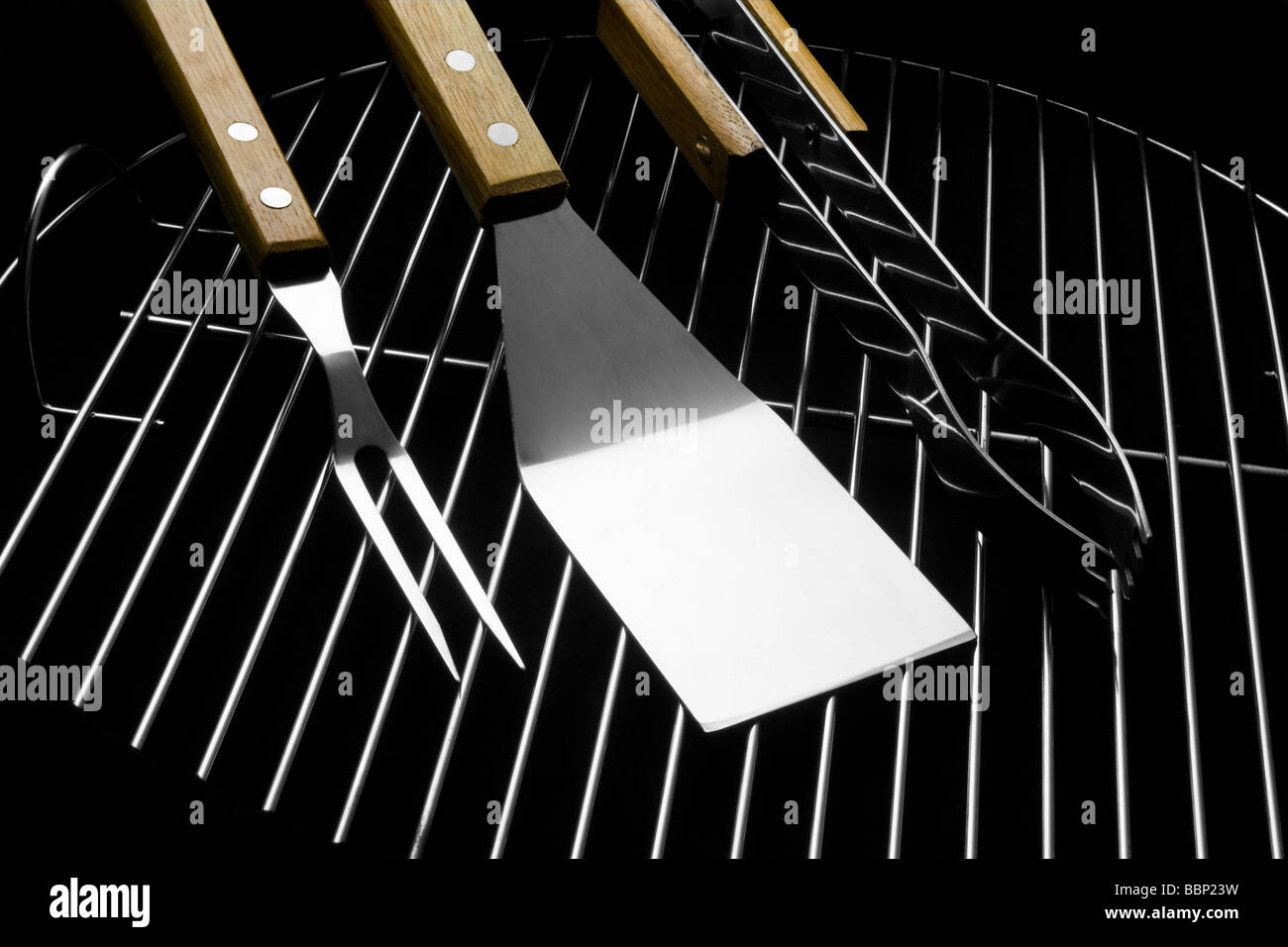 Three stainless steel barbecue utensils on grill. Fork, spatula, tongs. Studio shot on black background. Stock Photo