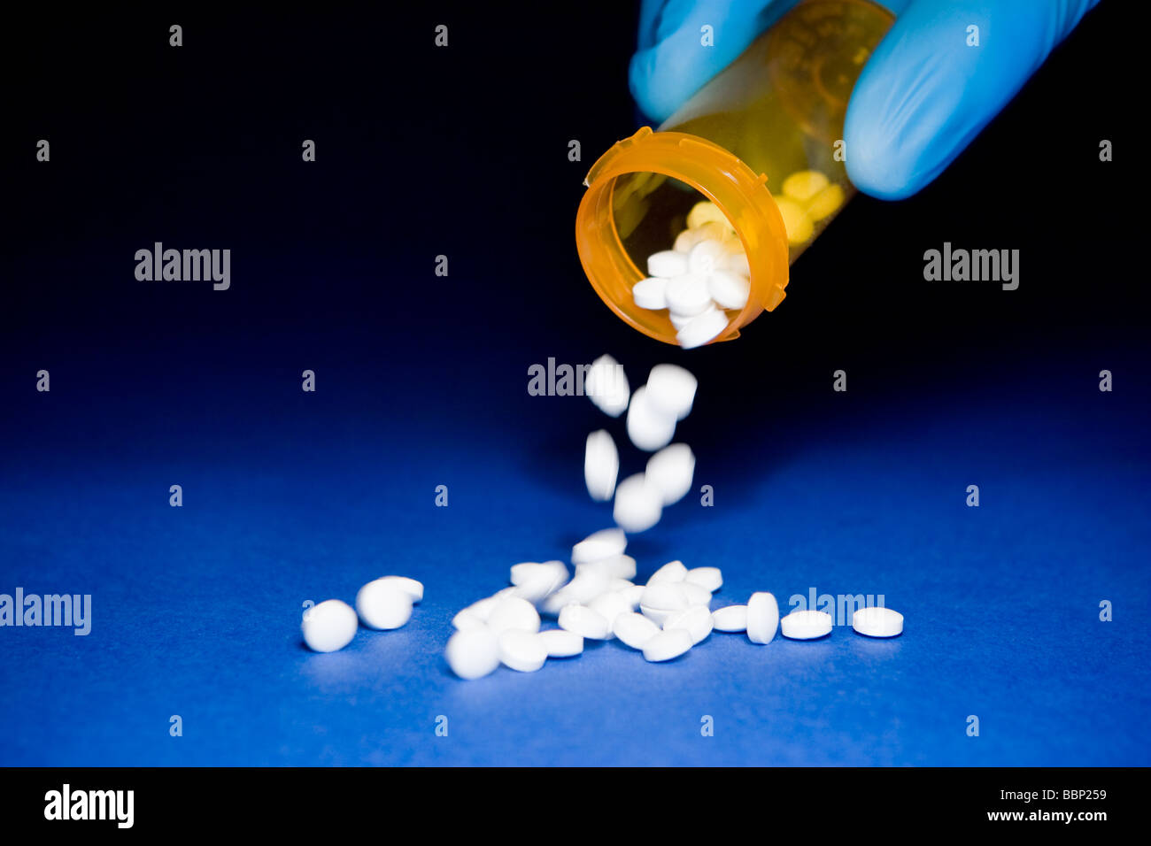 Close-up of a hand in a blue surgical glove emptying an orange prescription bottle of white pills Stock Photo