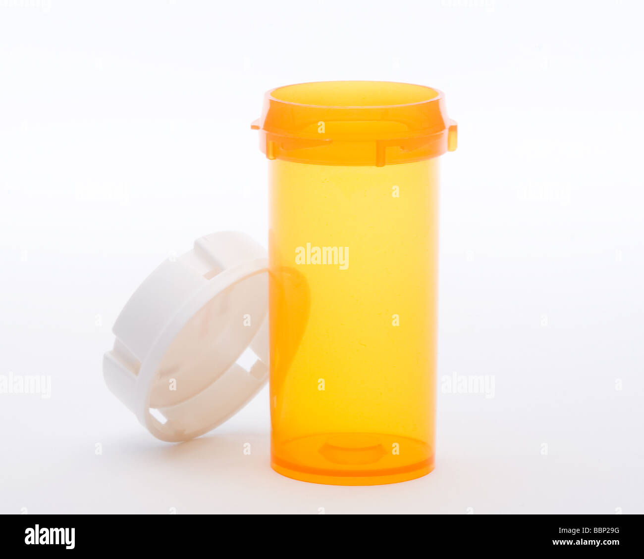 Empty orange pill bottle and white lid leaning against bottle. No labels on bottle, against white background Stock Photo