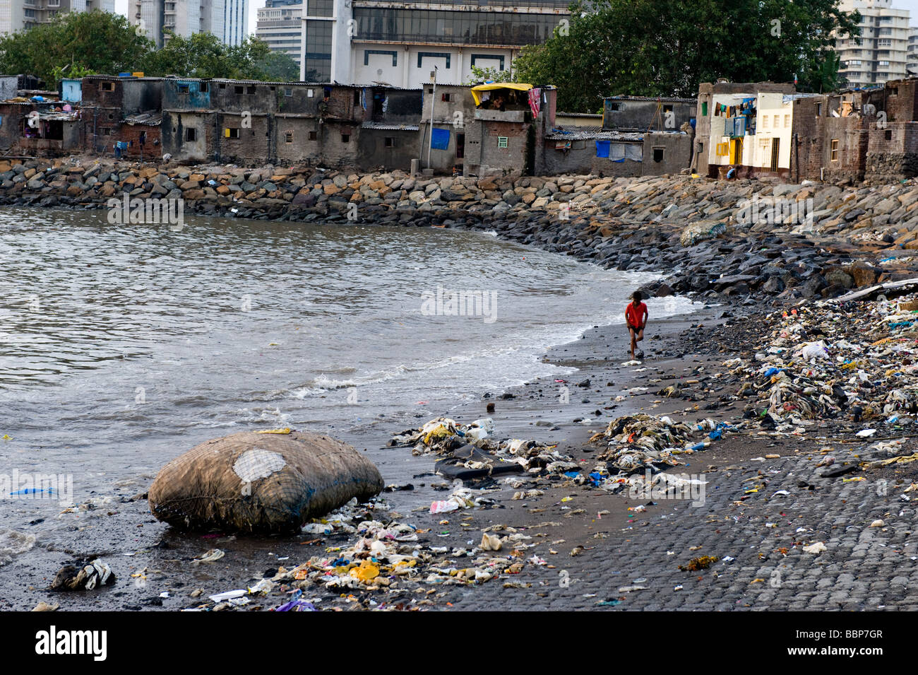 Boy walknig along a rubbish strewn beach in Mumbai, India Stock Photo