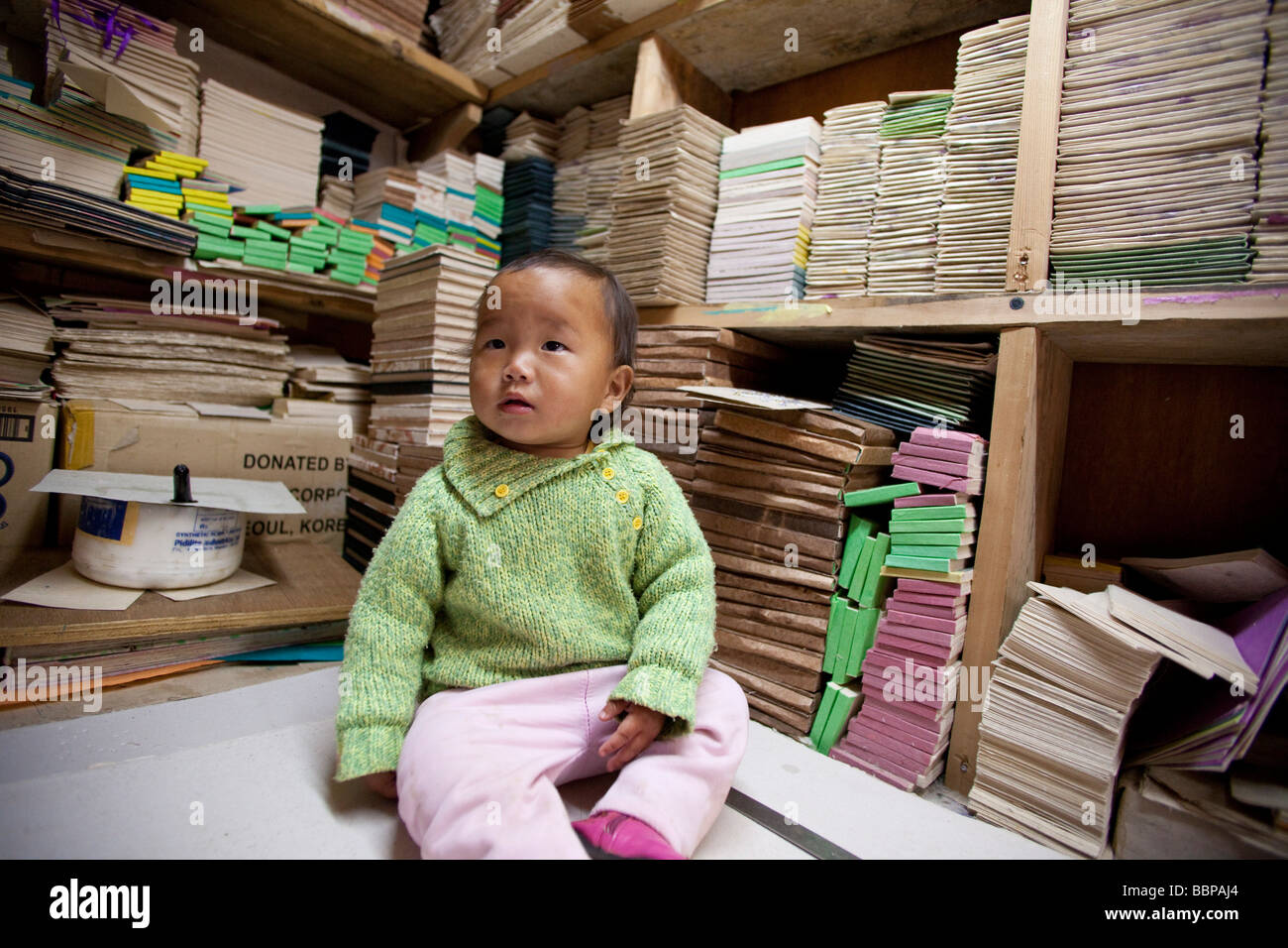 Young child baby  sitting on desk and books at Jungshi Handmade Paper Factory in Thimphu Bhutan, Asia 91039 Bhutan-Thimphu Stock Photo
