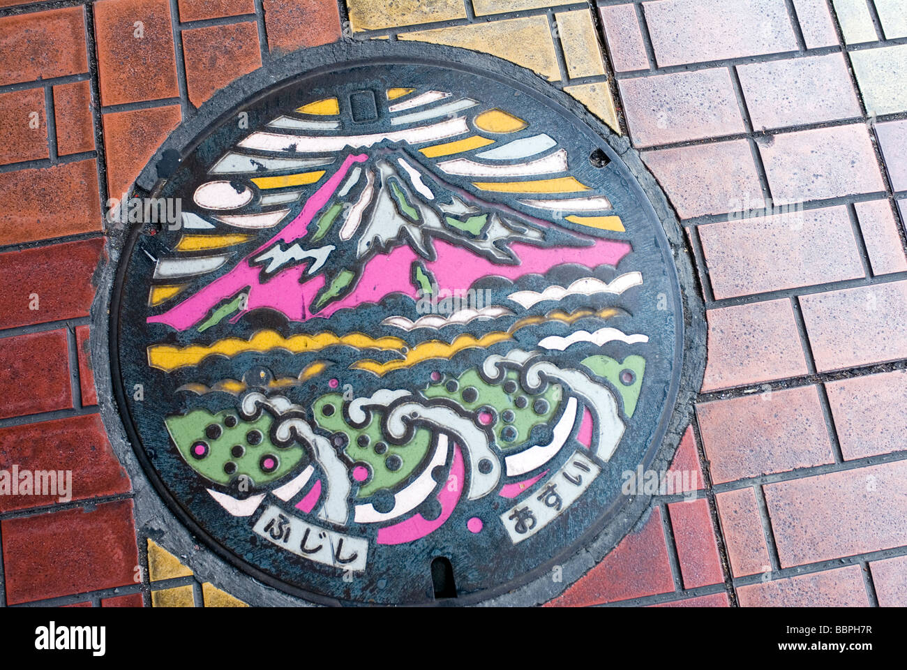 An artistic manhole cover showing Mount Fuji and Hokusai-like ocean waves on a sidewalk in Fuji City, Shizuoka Prefecture. Stock Photo