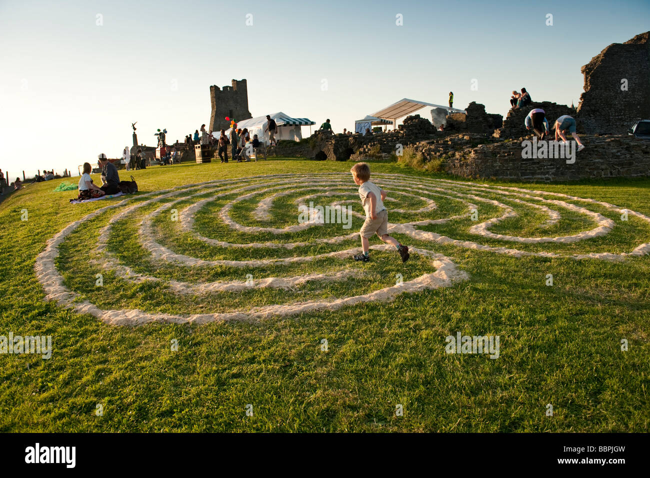 Young child running through a sawdust maze pattern on the grass at Roc y Castell Castle Rock free music festival Aberystwyth Stock Photo