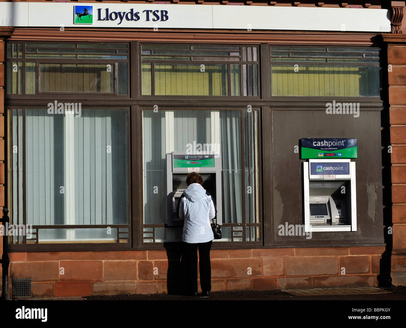 A women uses an ATM cashpoint at Lloyds TSB bank Stock Photo