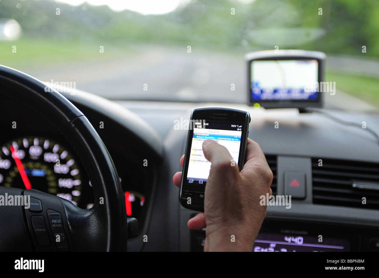 Man using a blackberry cell phone to check email while drive his car Stock Photo