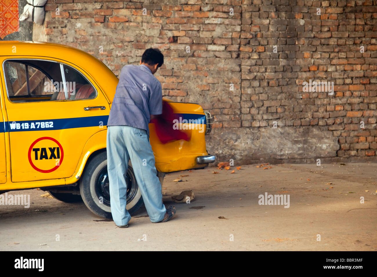 An Indian man cleans his yellow taxi, Kolkata, India Stock Photo