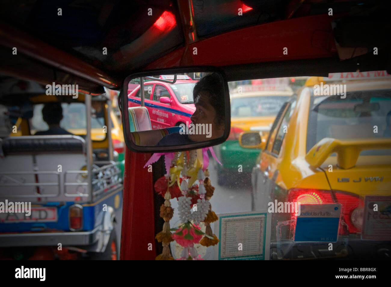 A driver is reflected in the rearview mirror of an Auto rickshaw taxi, commonly known as Tuk Tuk in Bangkok Thailand Stock Photo