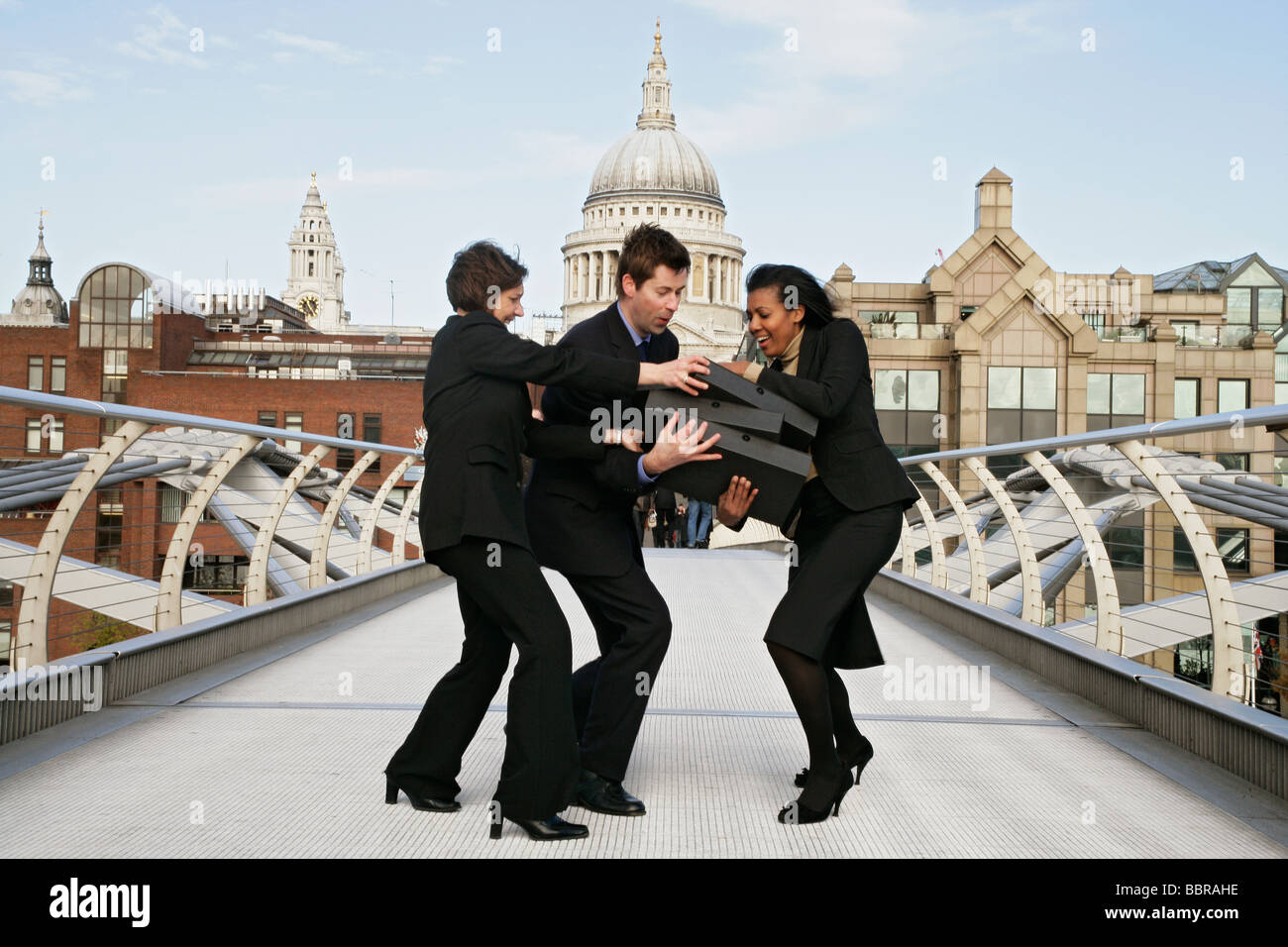 Three business people (two female, one male) on the millennium struggling to hold a pile of file boxes, Stock Photo