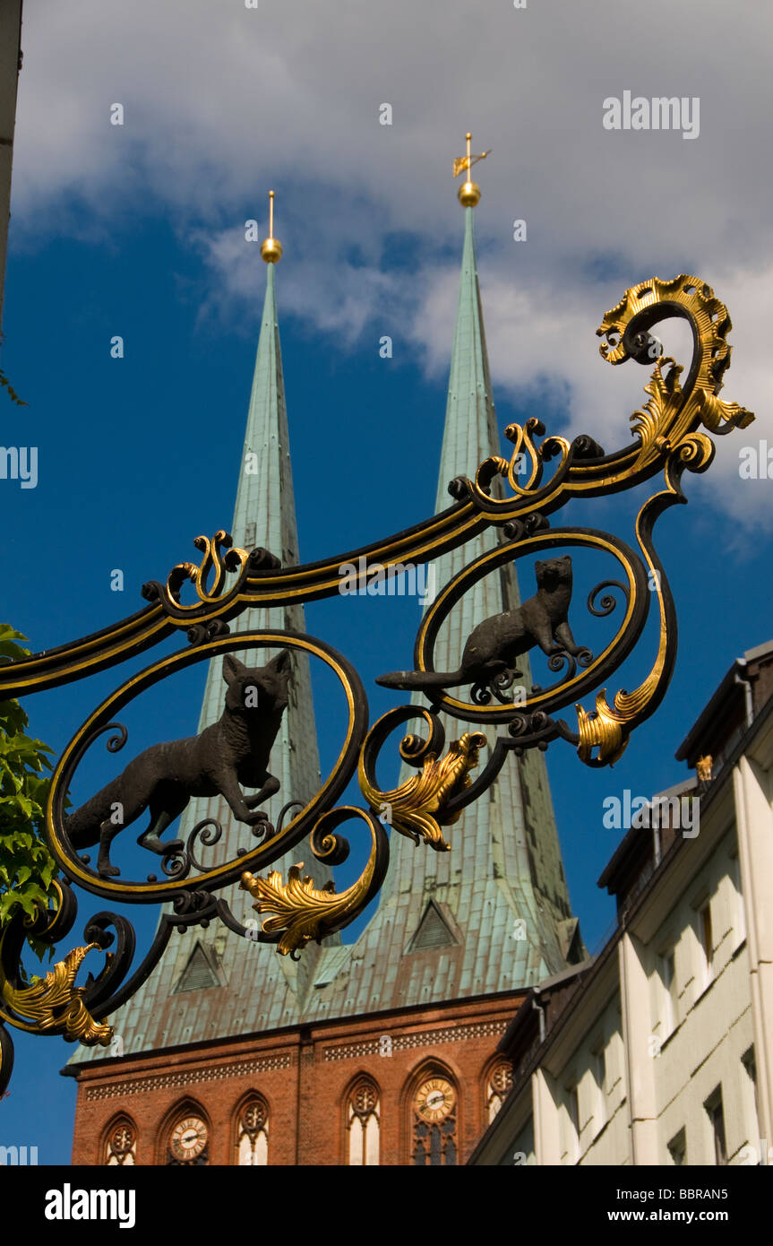Medieval wrought iron shop sign with spires of Nikolaikirche church in background Mitte Quarter Scheunenviertel Berlin Germany Stock Photo