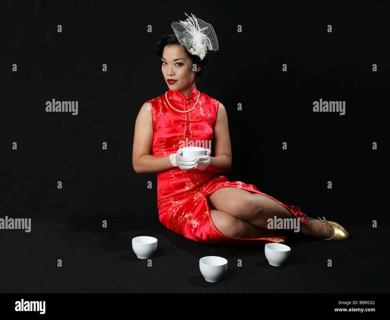 Pinup Portrait of Burlesque Performer Marianne Cheesecake in a Long Chinese Dress with White Hat and Gloves Holding a Teacup Stock Photo