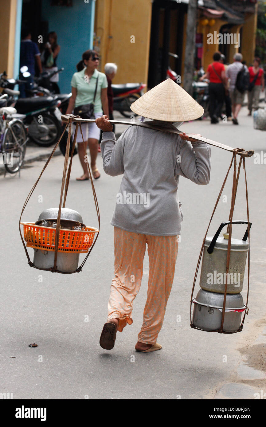 Vietnamese street scene, woman carrying metal pots in traditional 'don ganh', 'Hoi An', Vietnam Stock Photo