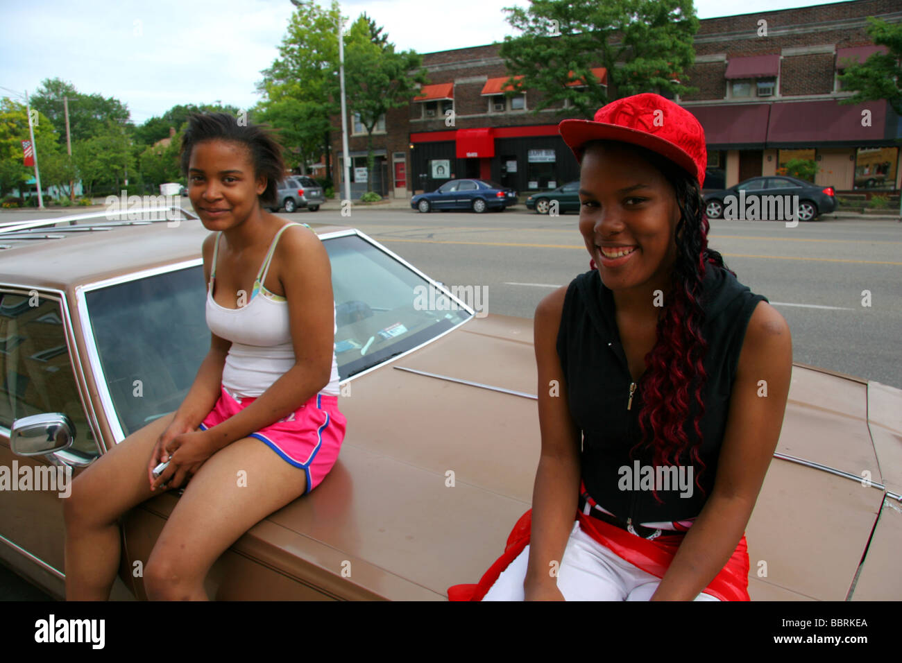 Two black girls sitting on a car in Detroit Michigan USA Stock Photo