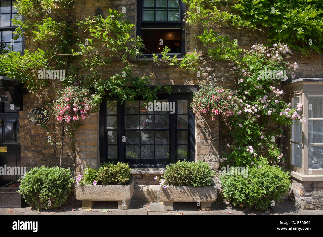 Quaint cottage view in Burford Oxfordshire, roses and shruberry surround the entrance door Stock Photo