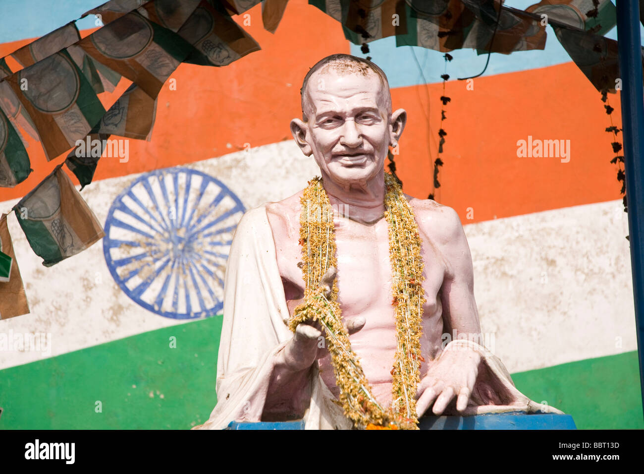 The garlanded statue of Mahatma Gandhi stands in front of the Indian flag. Stock Photo