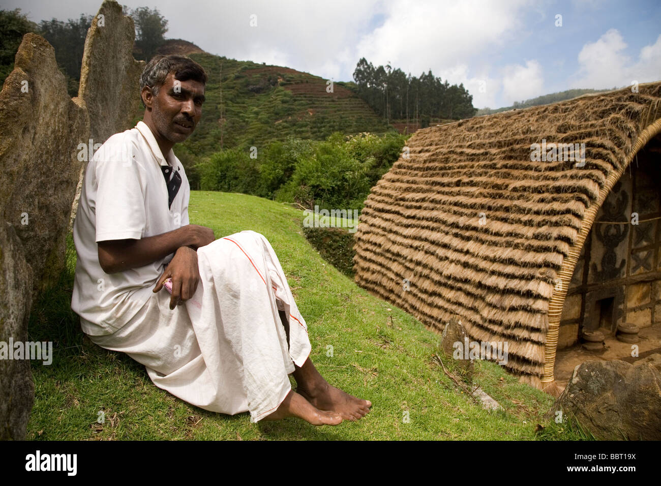 A man sits by a temple in a Toda tribal mund (settlement). The mund is within the Botanical Garden at Ooty. Stock Photo