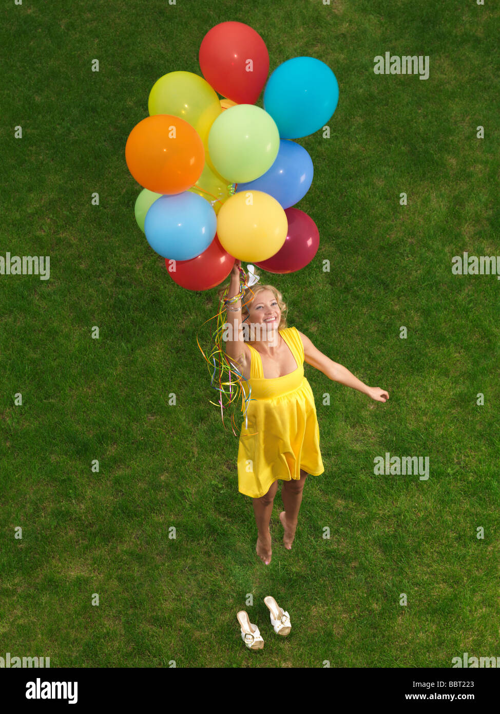 Young happy woman flying up from the ground on colorful air balloons Stock Photo