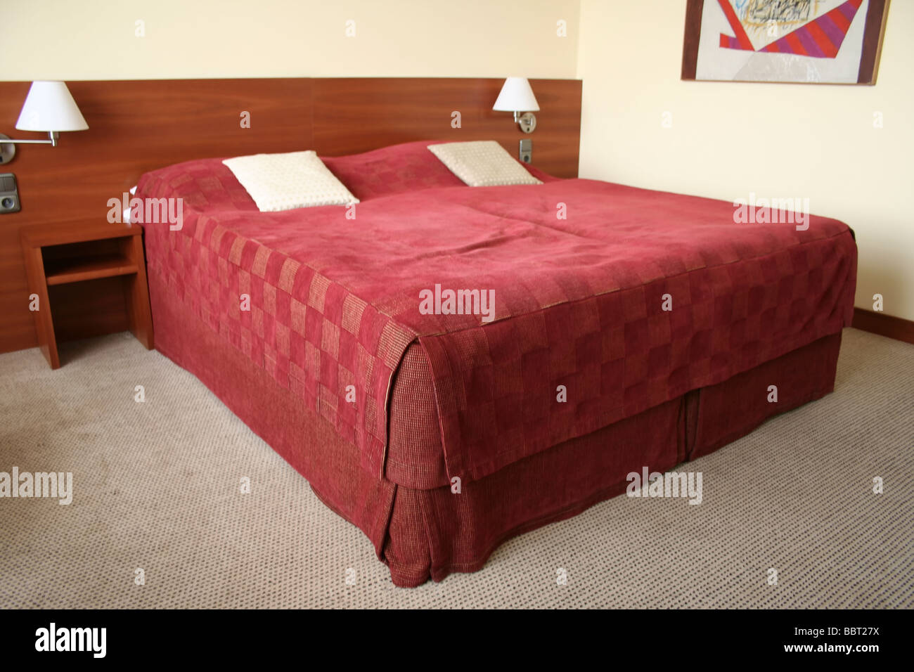 King size bed in a hotel room with a wooden bedhead and carpet on the