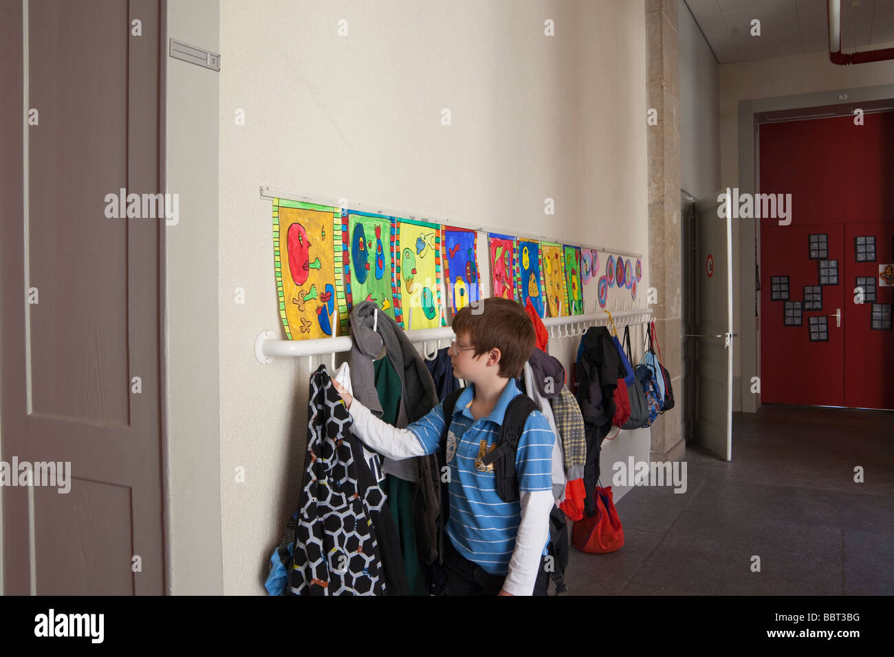 9 year old boy taking his coat off of a coat hook outside his classroom