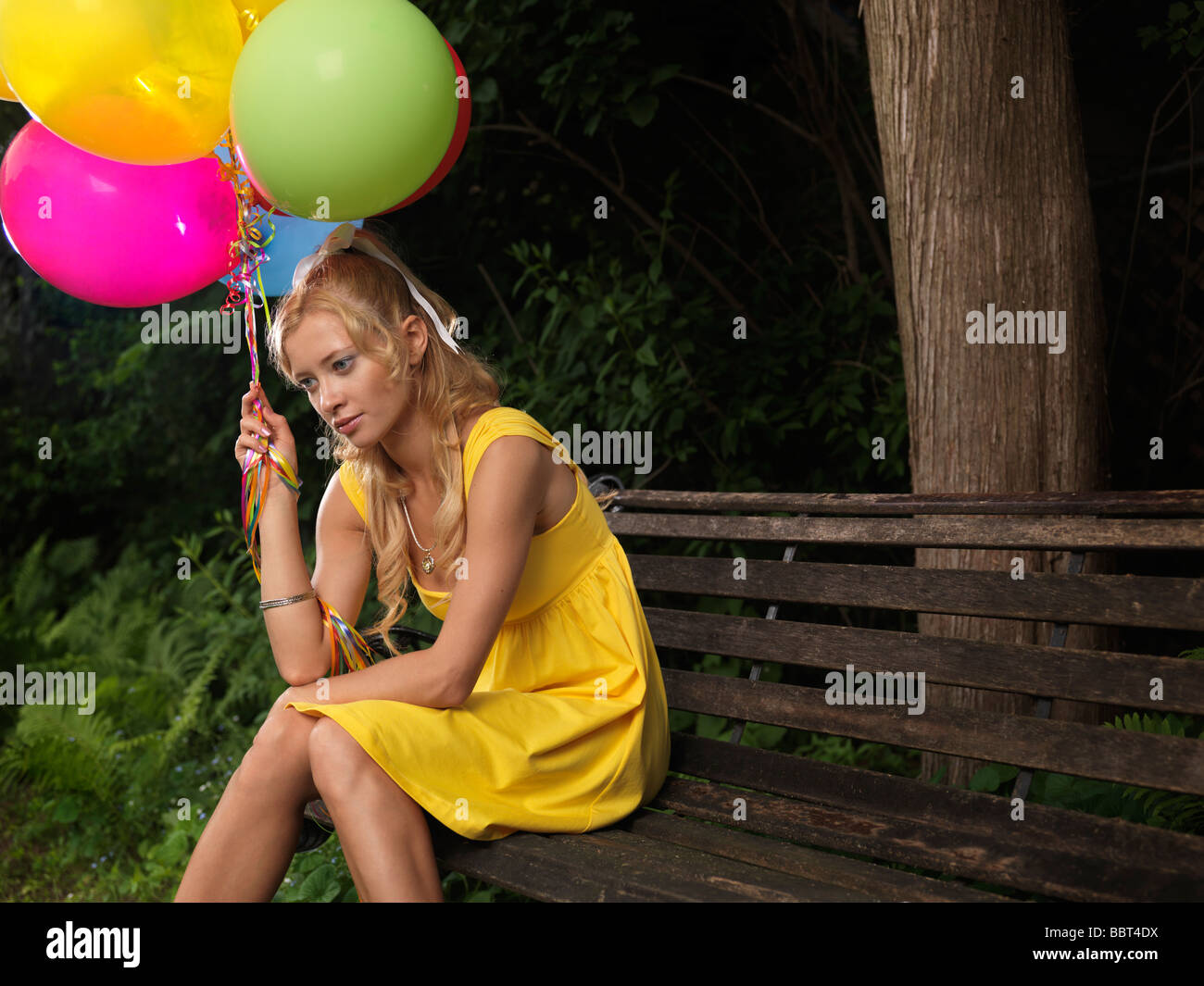 Young sad woman sitting on a bench with a bunch of colorful balloons Stock Photo