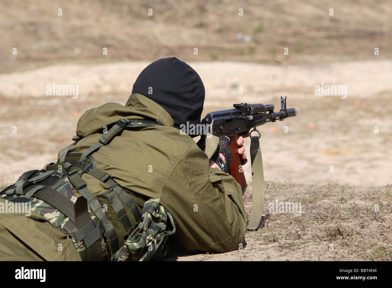 Terrorist dressed man in a balaclava firing an AK47 kalashnikov rifle and wearing a belt of bullets Stock Photo