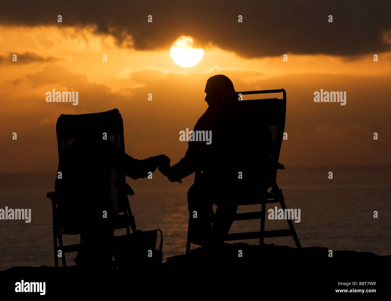 An elderly couple sitting in deck chairs watch a dramatic sunset over the sea from Cabo de São Vicente in the western Algarve Stock Photo