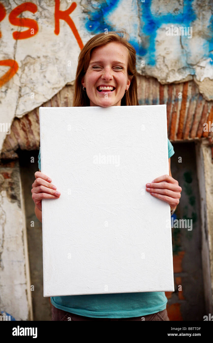 Young white woman holding blank white canvas sign in front of old wall ...