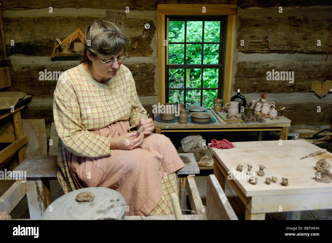 Woman In Pioneer Period Costume Working With Clay In Log Cabin At
