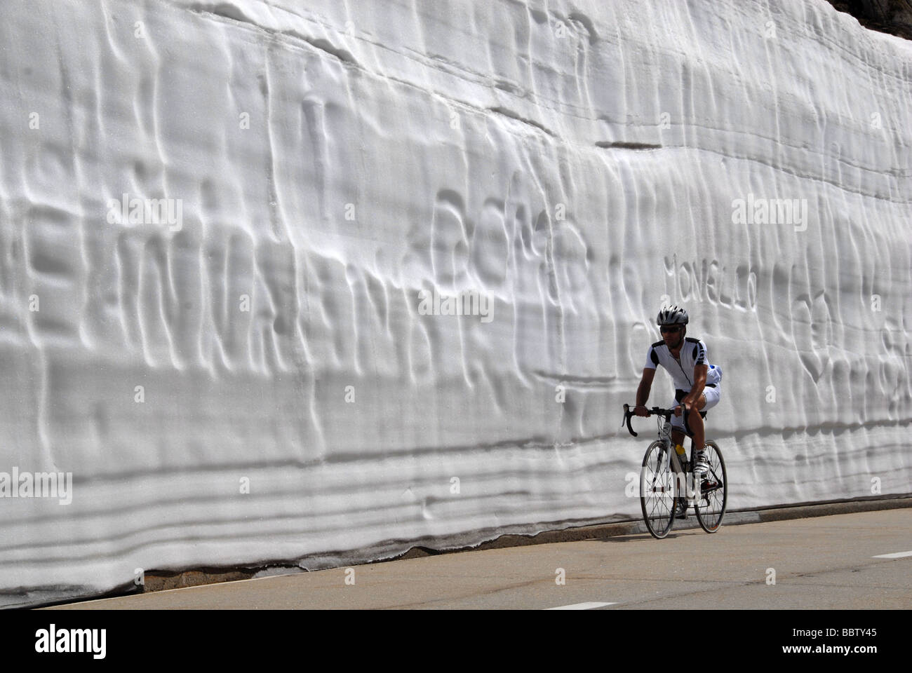 Bicycler riding under huge snow wall in spring on Nufenen Pass road Swiss alps Switzerland Stock Photo