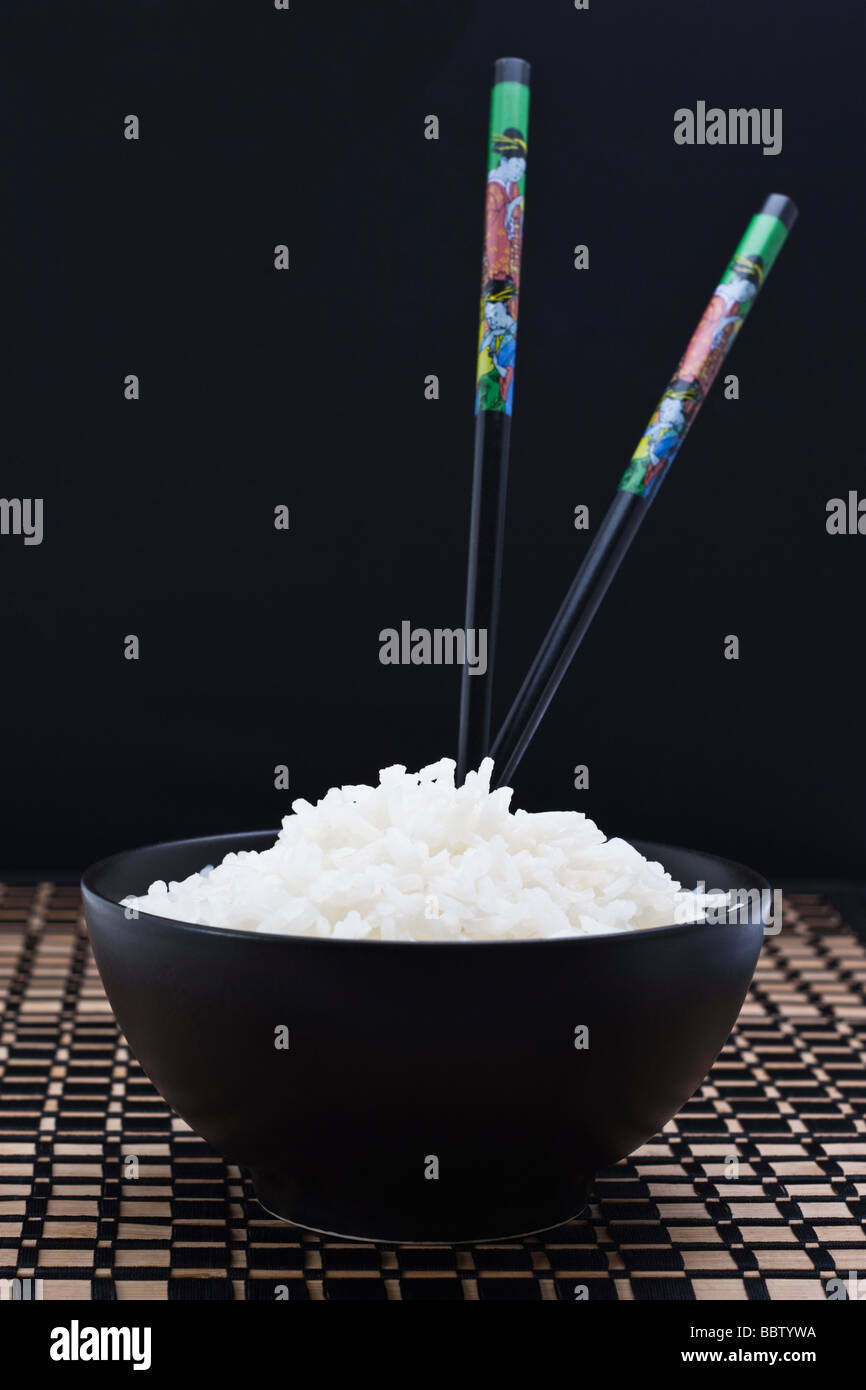 Boiled white rice in black dish with two chopsticks Stock Photo